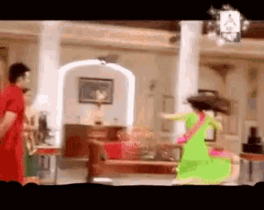 a woman in a green dress is dancing in a living room with a man in a red shirt behind her .