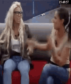 two women are sitting next to each other on a red couch and talking to each other .