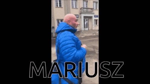 a man in a blue jacket stands in front of a building with the name smariuszki written on the bottom