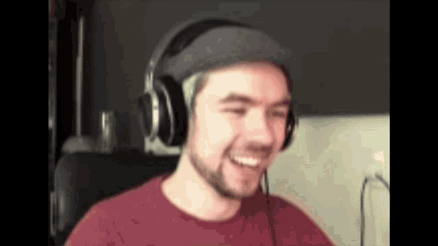 a man wearing headphones and a hat is smiling while sitting at a desk .