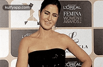 a woman in a black strapless dress is standing in front of a wall with a sign that says l' oreal .