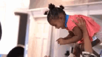 a little girl in a pink dress is being lifted in the air by a man .