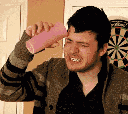 a man drinking from a pink cup in front of a dartboard