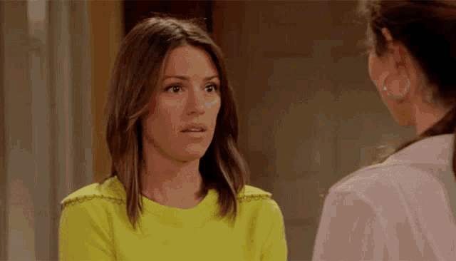 a woman in a yellow shirt is talking to another woman in a pink shirt .