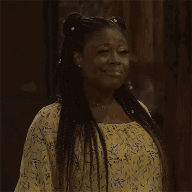 a woman with braids is wearing a yellow floral top and smiling .