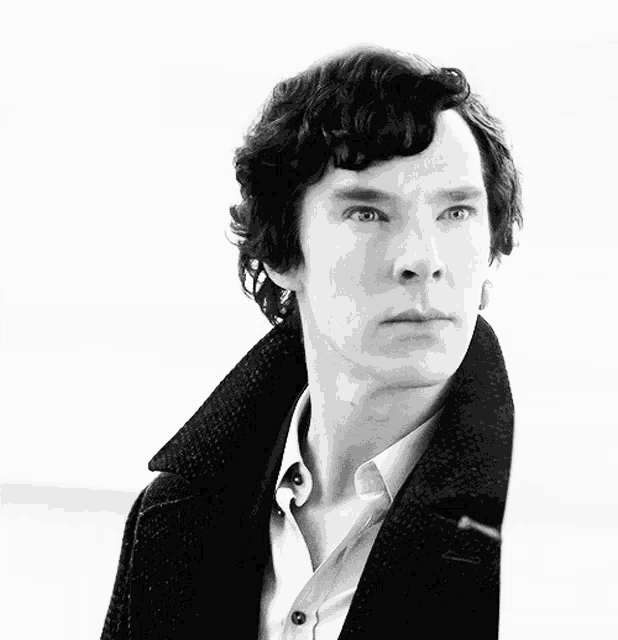 a man with curly hair wearing a black coat and white shirt