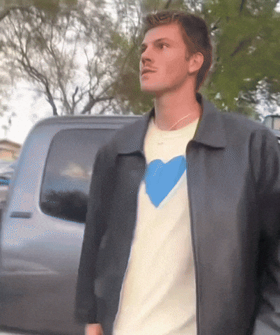 a man wearing a white shirt with a blue heart on it is standing in front of a truck