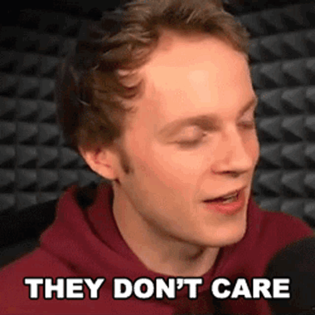 a man in a red hoodie is talking into a microphone with the words they don 't care above him