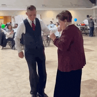 a man in a suit and tie is dancing with an older woman in a maroon jacket