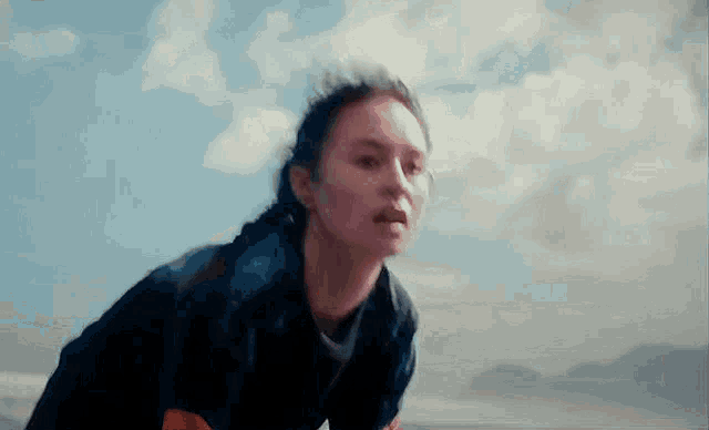 a woman in a black jacket is running on a beach with a blue sky in the background .
