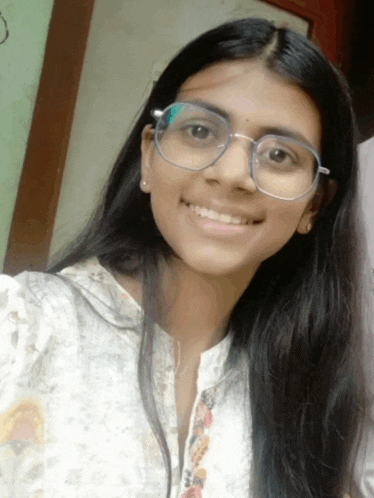 a young woman wearing glasses and a white shirt smiles for the camera