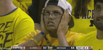a person wearing glasses and a baseball cap is watching a game between michigan and illinois
