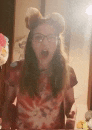 a woman wearing a tie dye shirt and mouse ears is standing in front of a mirror .