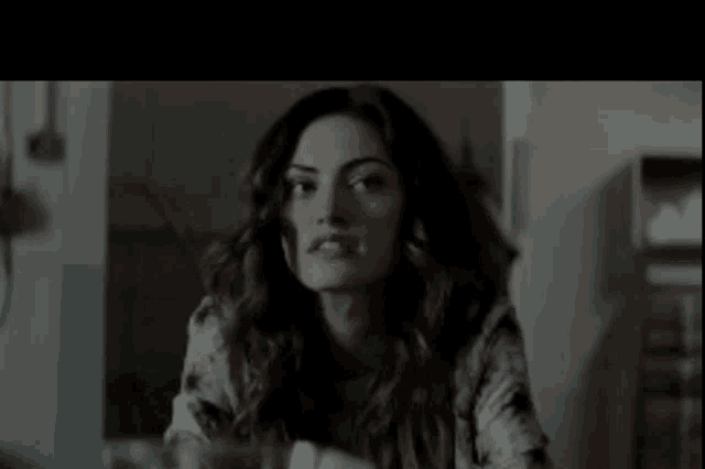 a woman with long hair is sitting in a dark room looking at the camera .