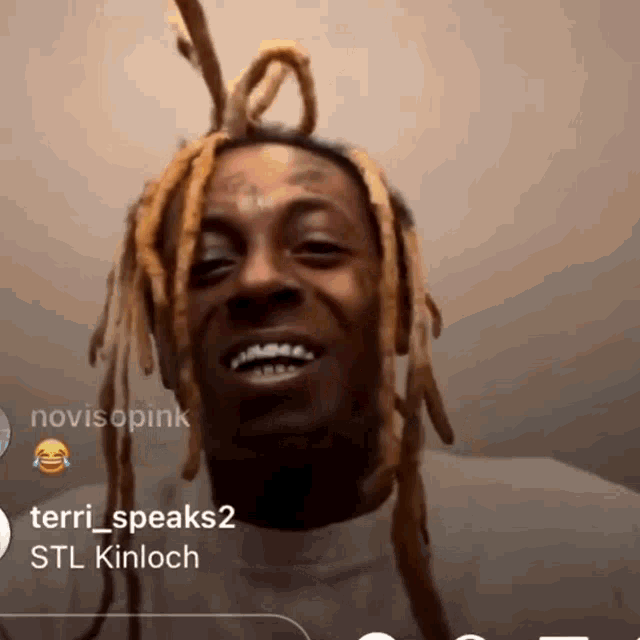 a man with blonde dreadlocks is smiling in front of a wall