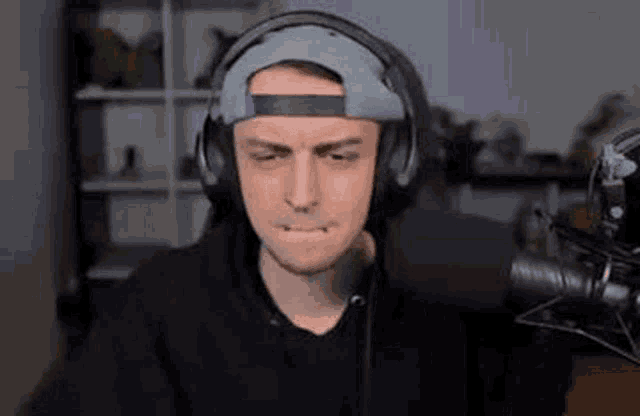 a man wearing headphones and a hat is making a funny face while sitting in front of a microphone .