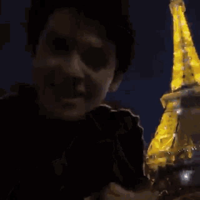a person is standing in front of the eiffel tower at night .