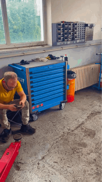 a man in a yellow shirt sits in front of a blue box that says elite