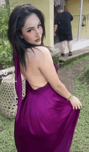a woman in a purple dress is posing for a picture while a man stands behind her .