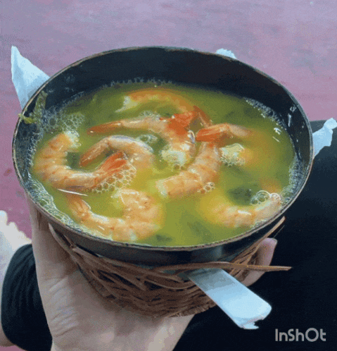 a person is holding a bowl of soup with shrimp in their hand