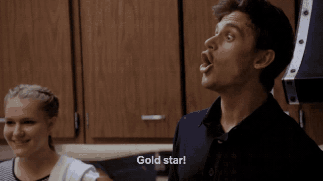 a man and a woman are standing in a kitchen and the man is saying gold star