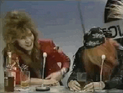 a man and a woman are sitting at a table with microphones and drinking beer .