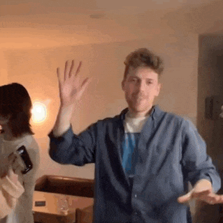 a man in a blue shirt is dancing in a living room while a woman watches .