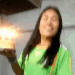 a woman in a green shirt is smiling and holding a candle