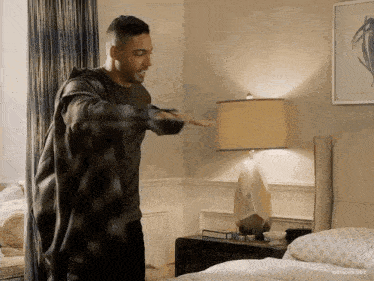 a man in a plaid shirt is standing next to a bed in a bedroom