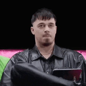 a man in a black leather jacket is sitting on a couch holding a tablet .