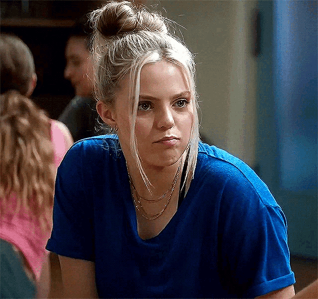 a woman with blonde hair in a bun is wearing a blue t-shirt .