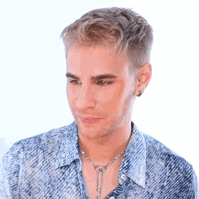 a man with blonde hair wearing a blue shirt and a silver necklace