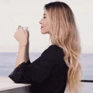 a woman is sitting on a balcony holding a cup of coffee and looking at the ocean .
