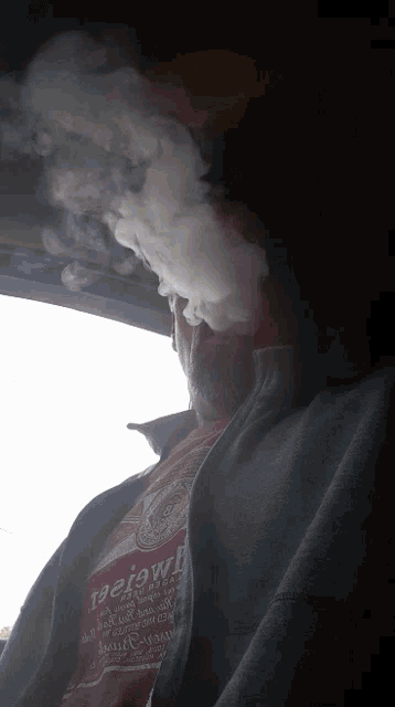 a man smoking a cigarette in a car wearing a red shirt that says review