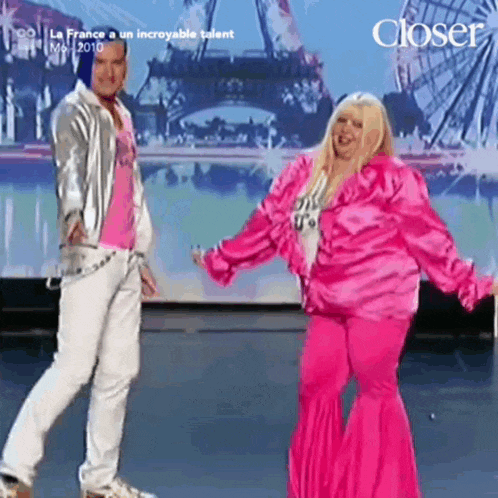a woman in a pink outfit is dancing with a man in a silver jacket in front of an eiffel tower