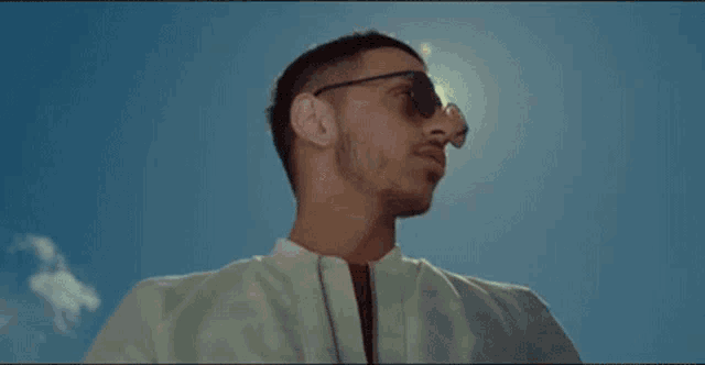 a man wearing sunglasses is standing in front of a blue sky with the sun shining on his face .