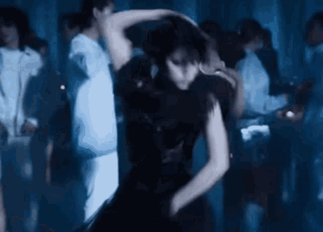 a woman in a black dress is dancing in a dark room with a crowd of people .
