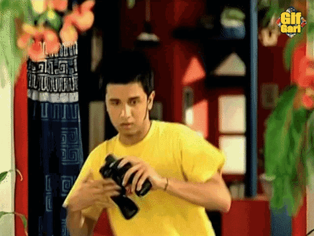 a man in a yellow shirt is holding a camera with a gif card logo in the background