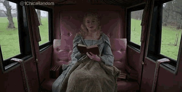 a woman is reading a book while sitting in a pink carriage .
