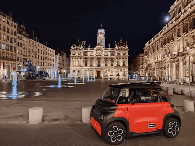 a small red car is parked in front of a fountain