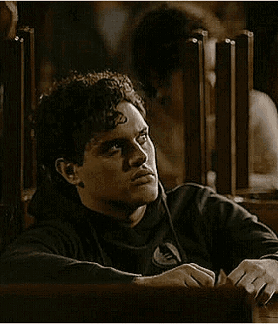 a young man is sitting at a table in a dark room with his head resting on a wooden table .