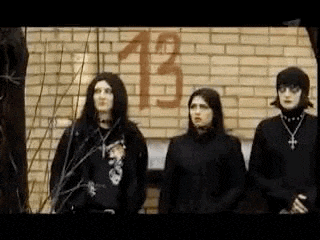 a group of people are standing in front of a brick wall with the number 13 painted on it .