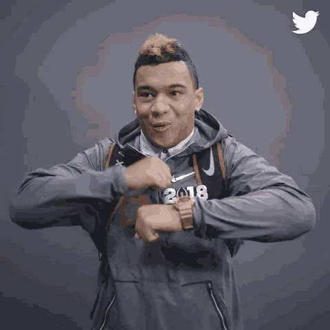 a man wearing a hoodie and a watch is making a funny face while holding his hands together .
