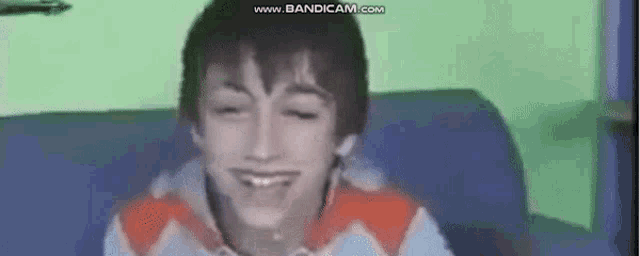 a young boy is smiling while sitting on a blue couch .