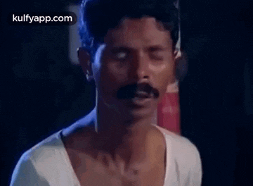 a man with a mustache is making a funny face with his eyes closed in a dark room .