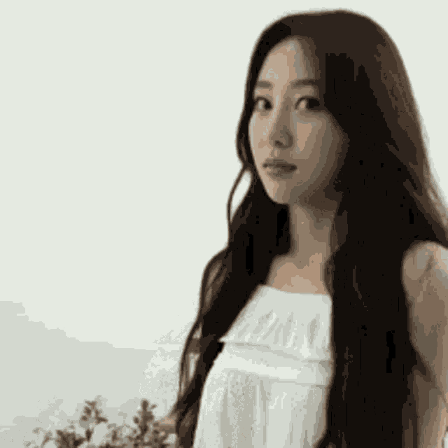 a woman with long hair is standing in front of a white wall holding a bouquet of flowers .