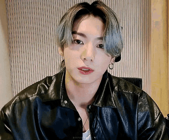 a young man with gray hair is wearing a black leather jacket and earrings .