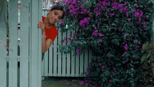 a woman in a red shirt peeking over a white fence