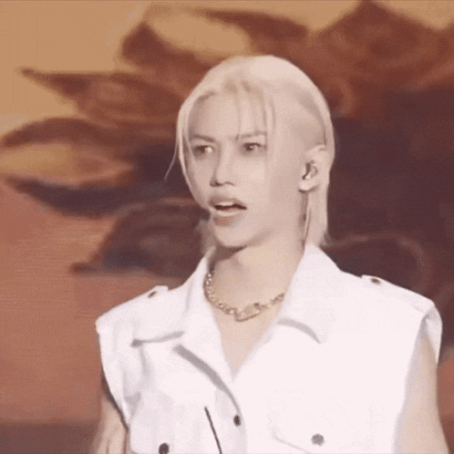 a man with blonde hair is wearing a white vest and a gold necklace .
