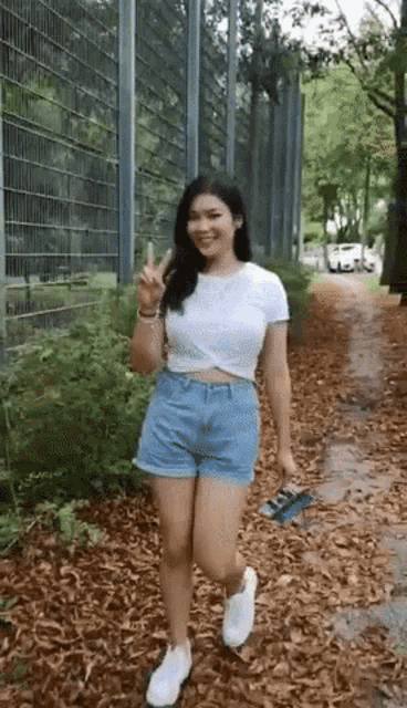 a woman in a white crop top and blue shorts is standing on a path .